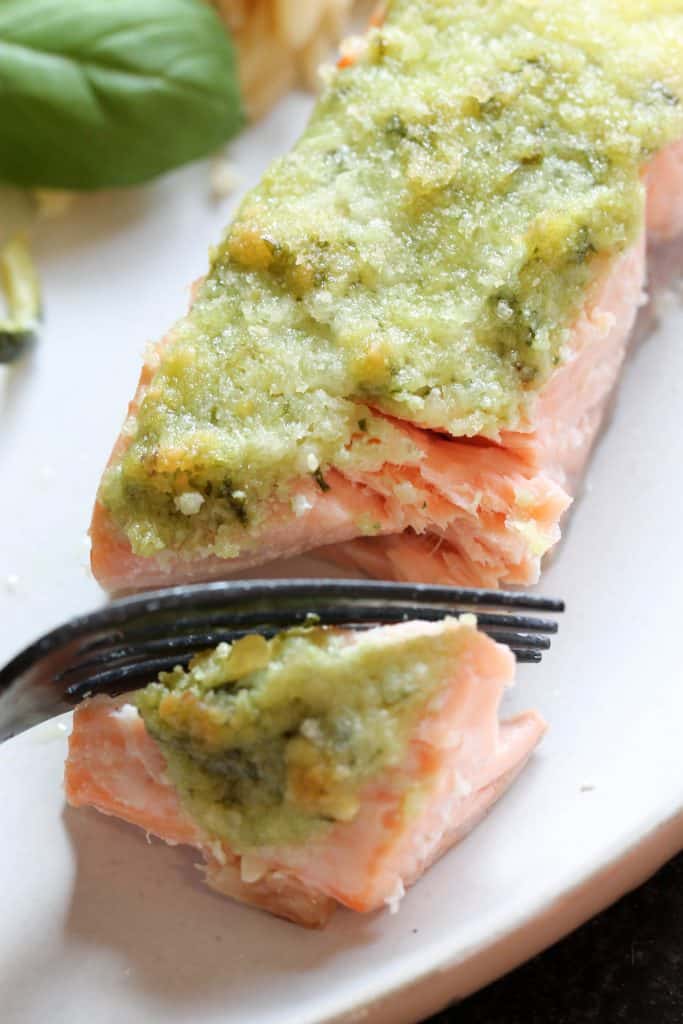 salmon filet with pesto on top being cut with a fork