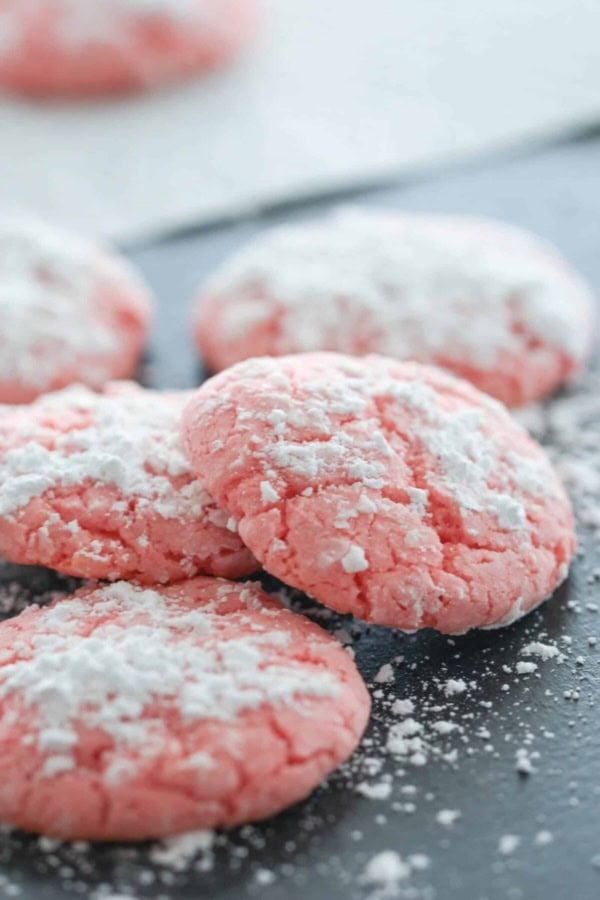 Strawberry Crinkle Cookies on a baking sheet dusted with powdered sugar with two cookies slightly stacked.