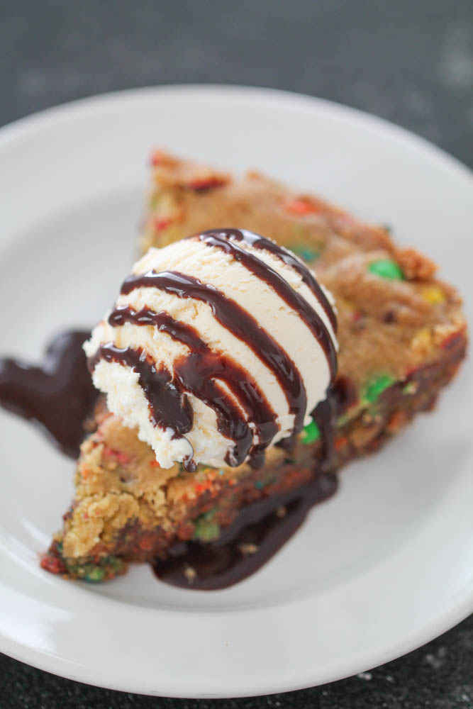 M&M Cookie Pie slice on a white plate with ice cream and chocolate sauce