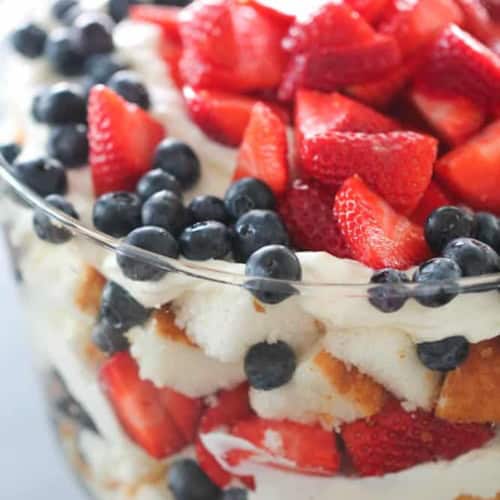 A glass trifle dish filled with layers of strawberries, blueberries, whipped cream, and sponge cake.