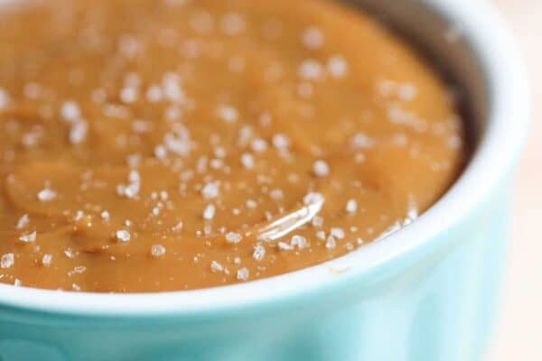 A close-up of a light blue ramekin filled with caramel sauce topped with coarse sea salt.