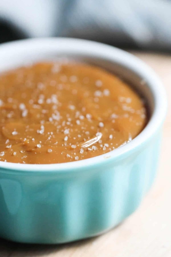 A close-up of a light blue ramekin filled with caramel sauce topped with coarse sea salt.
