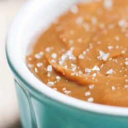 Close-up of salted caramel sauce in a light blue ceramic dish, topped with coarse sea salt crystals.