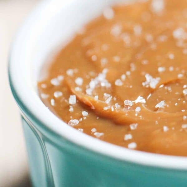 Close-up of salted caramel sauce in a light blue ceramic dish, topped with coarse sea salt crystals.
