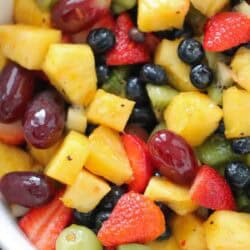 A bowl filled with a mixed fruit salad containing pineapple chunks, strawberries, blueberries, grapes, and kiwi slices.
