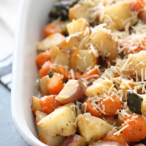 A white baking dish filled with roasted potatoes, carrots, and zucchini, topped with shredded cheese.