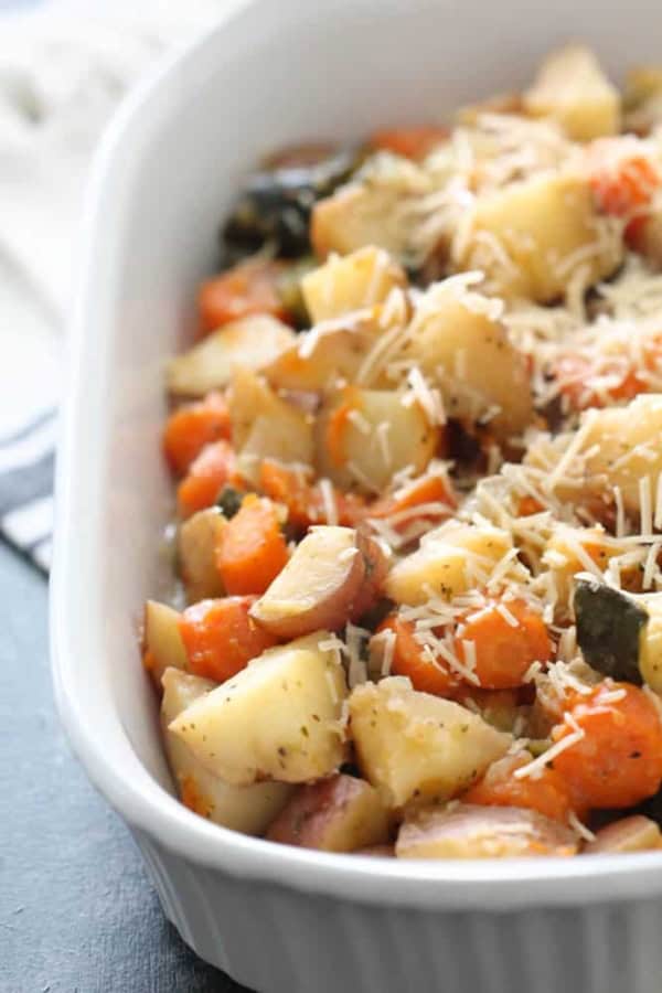A white baking dish filled with roasted potatoes, carrots, and zucchini, topped with shredded cheese.