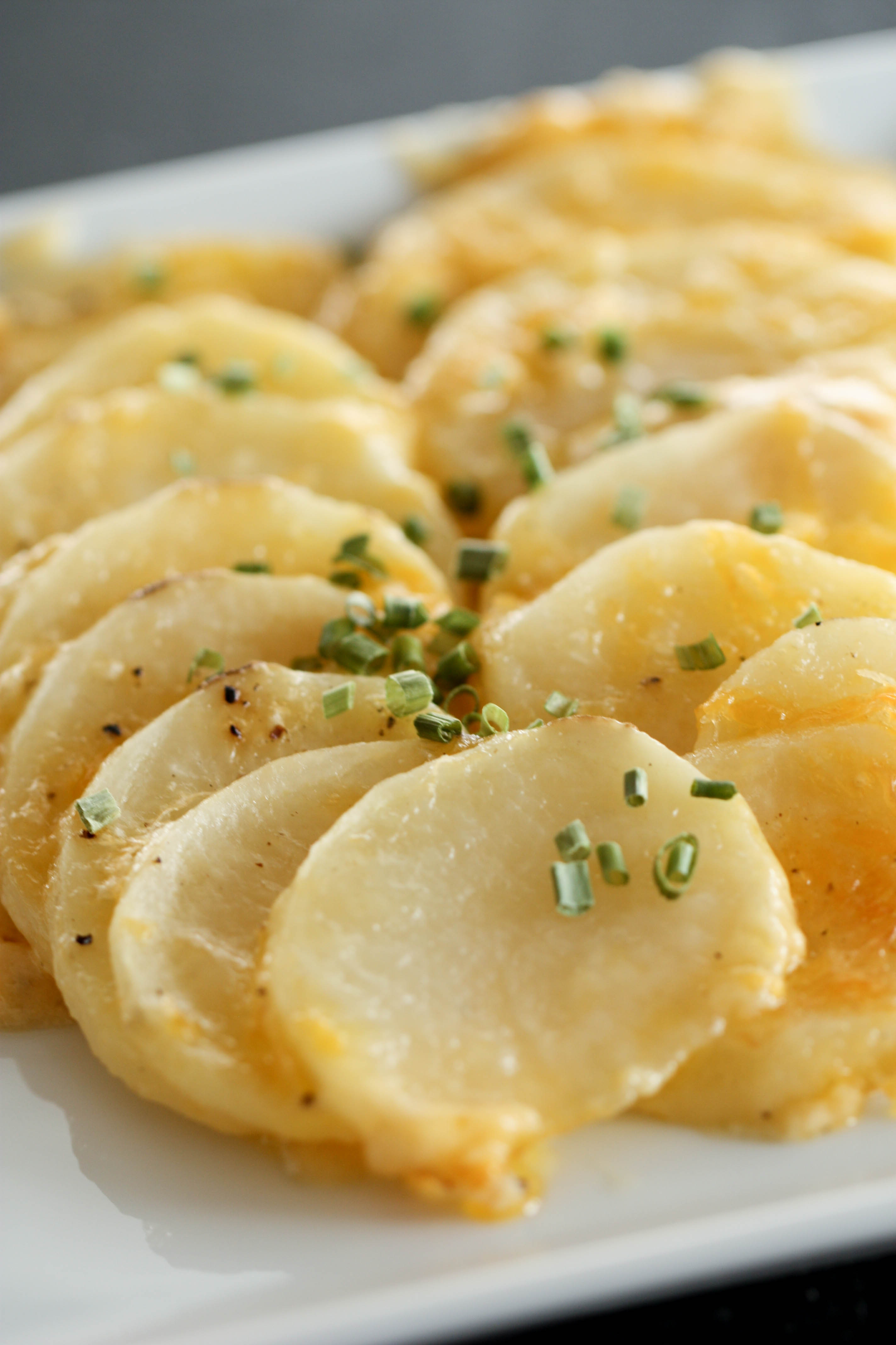 sliced cheesy potatoes with chives on top on a white platter