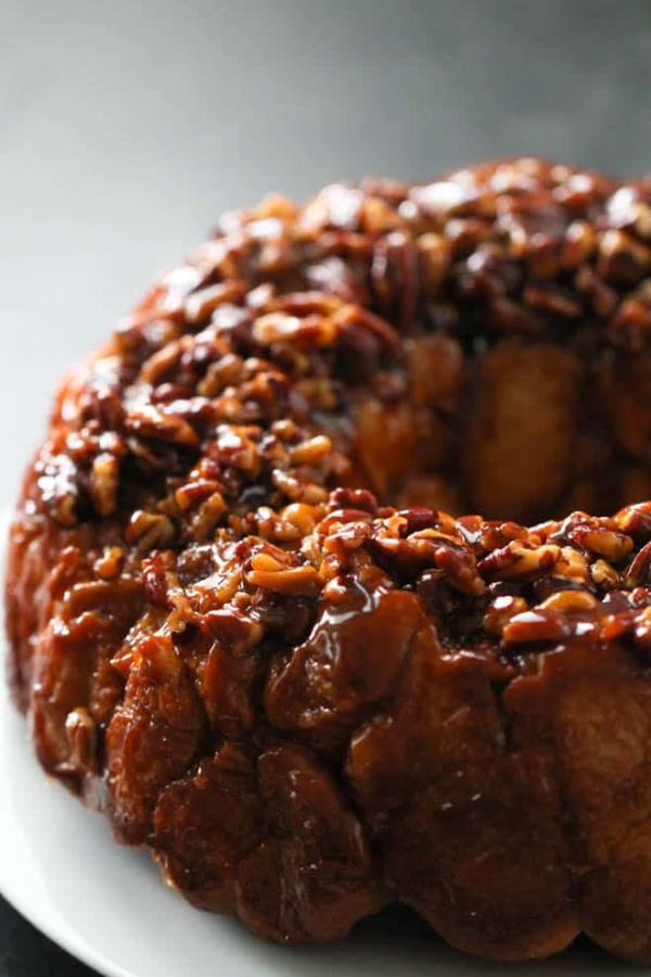 A close-up photo of a sticky, glazed monkey bread covered with chopped pecans on a white plate.