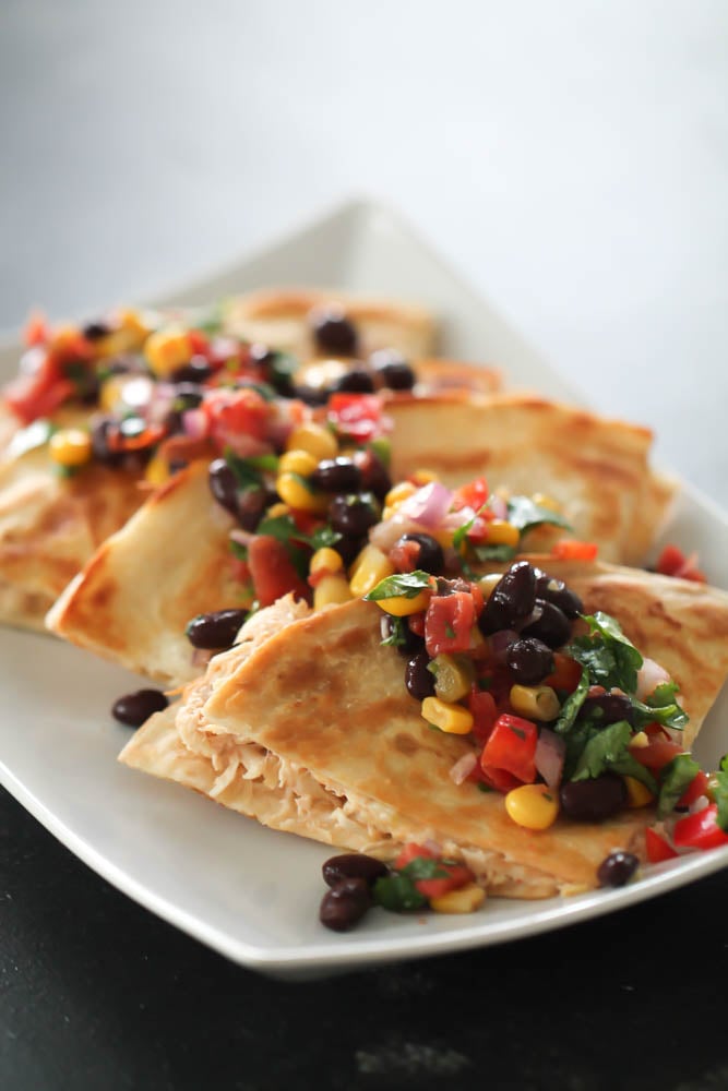 Slow Cooker Cheesy Chicken Quesadillas cut into triangles served on a plate topped with black bean and corn salsa