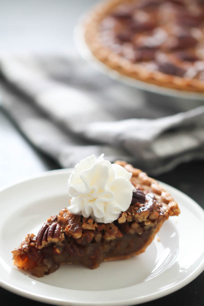 Slice of Easy Pecan Pie Recipe on a white plate topped with whip cream