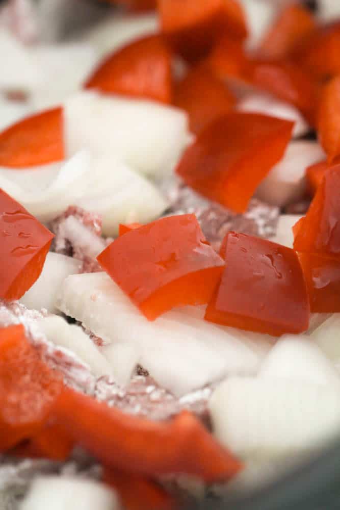 Chopped Onions and Peppers on top of uncooked beef in slow cooker