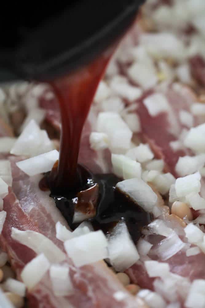 Pouring sauce over beans, bacon and onion