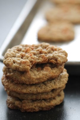 Close-up of a stack of four oatmeal cookies in front of a baking tray with more cookies.
