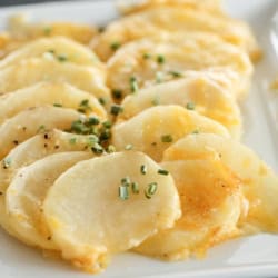 A plate of thinly sliced, cooked potatoes garnished with finely chopped green herbs.