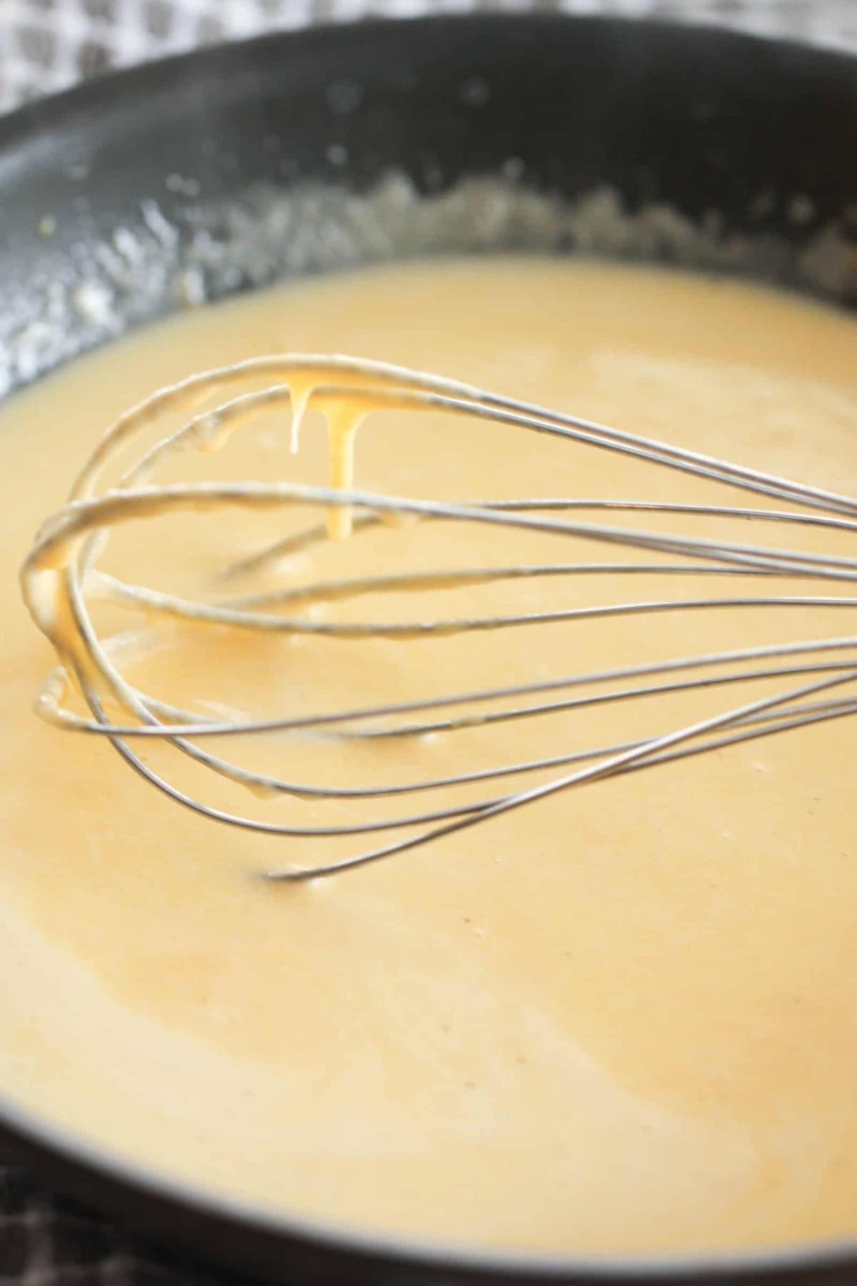 A metal whisk rests in a pan filled with smooth, light brown sauce.