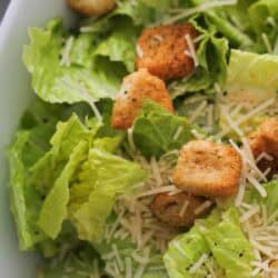 Close-up of a Caesar salad with romaine lettuce, shredded Parmesan cheese, and seasoned croutons in a white bowl.