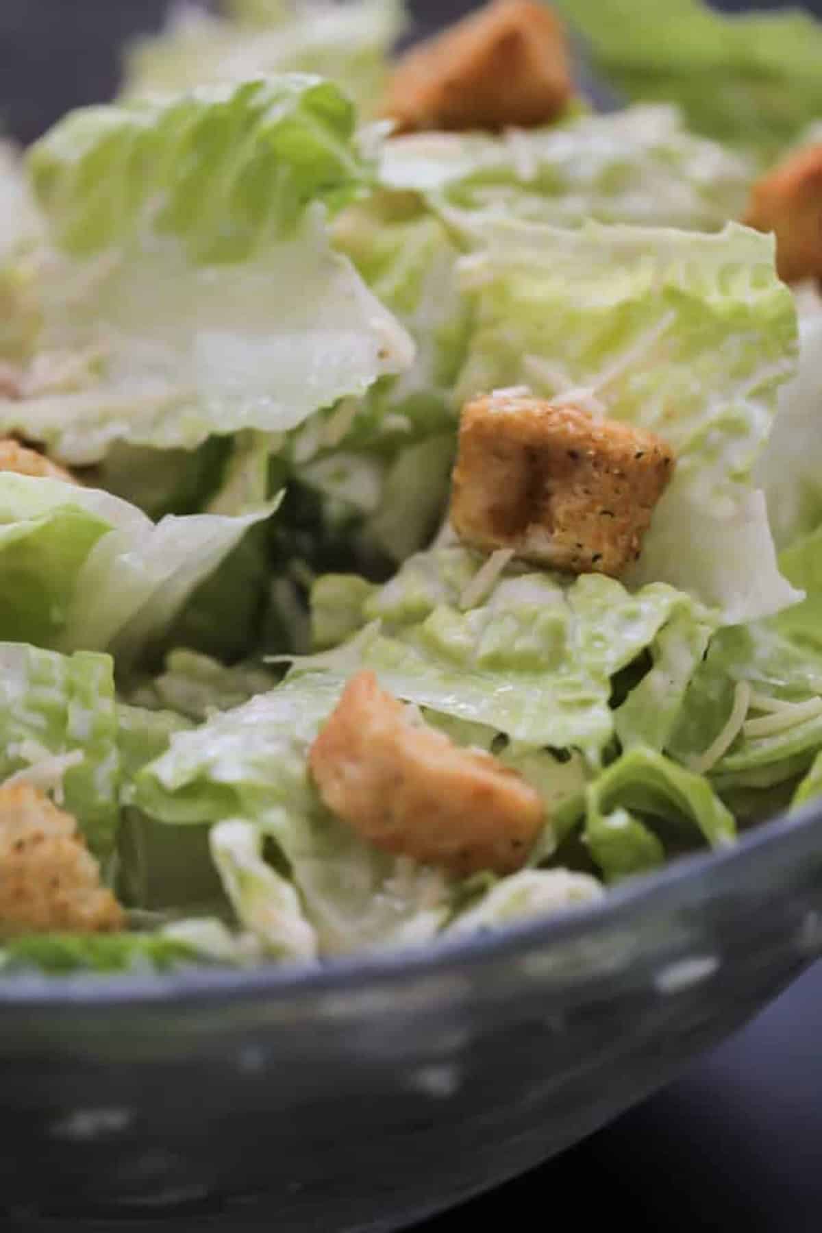 Close-up of a Caesar salad with romaine lettuce, croutons, and grated cheese in a glass bowl.