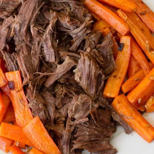 Tender shredded beef with roasted carrots on a white plate.