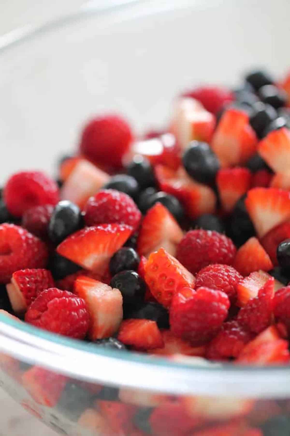Strawberries, blueberries and raspberries mixed together in a glass mixing bowl.
