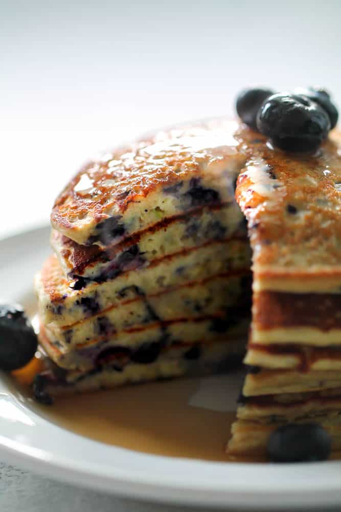 Blueberry Protein Pancakes stacked on a white plate with syrup on top