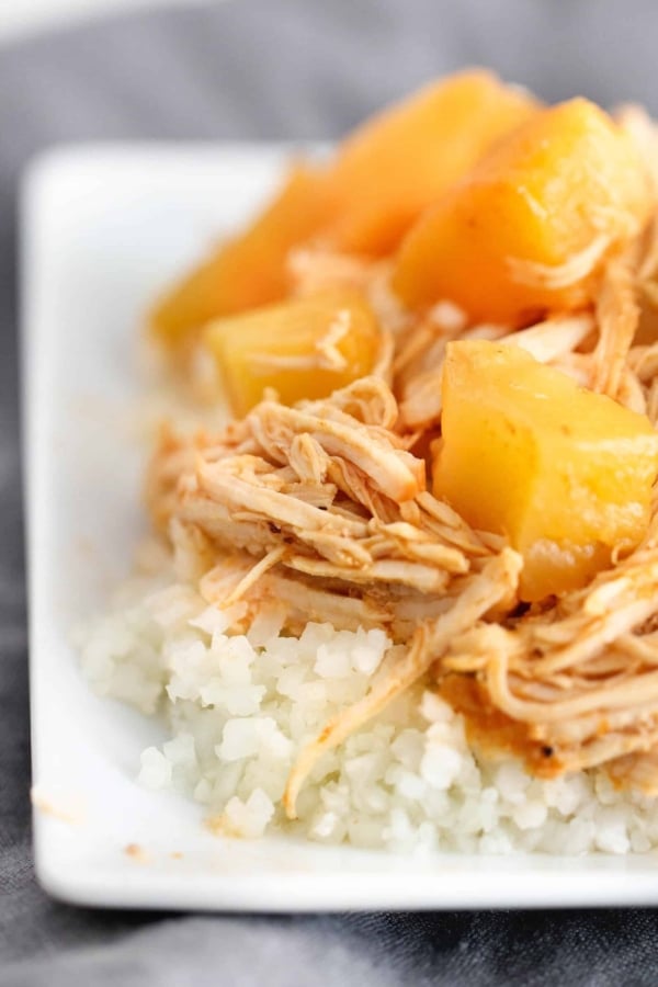 Shredded chicken and pineapple chunks served over a bed of white rice on a white plate.