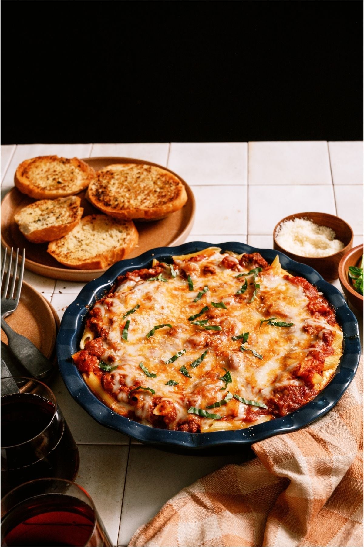Baked Ziti in a round baking dish with a plate of garlic bread on the side.
