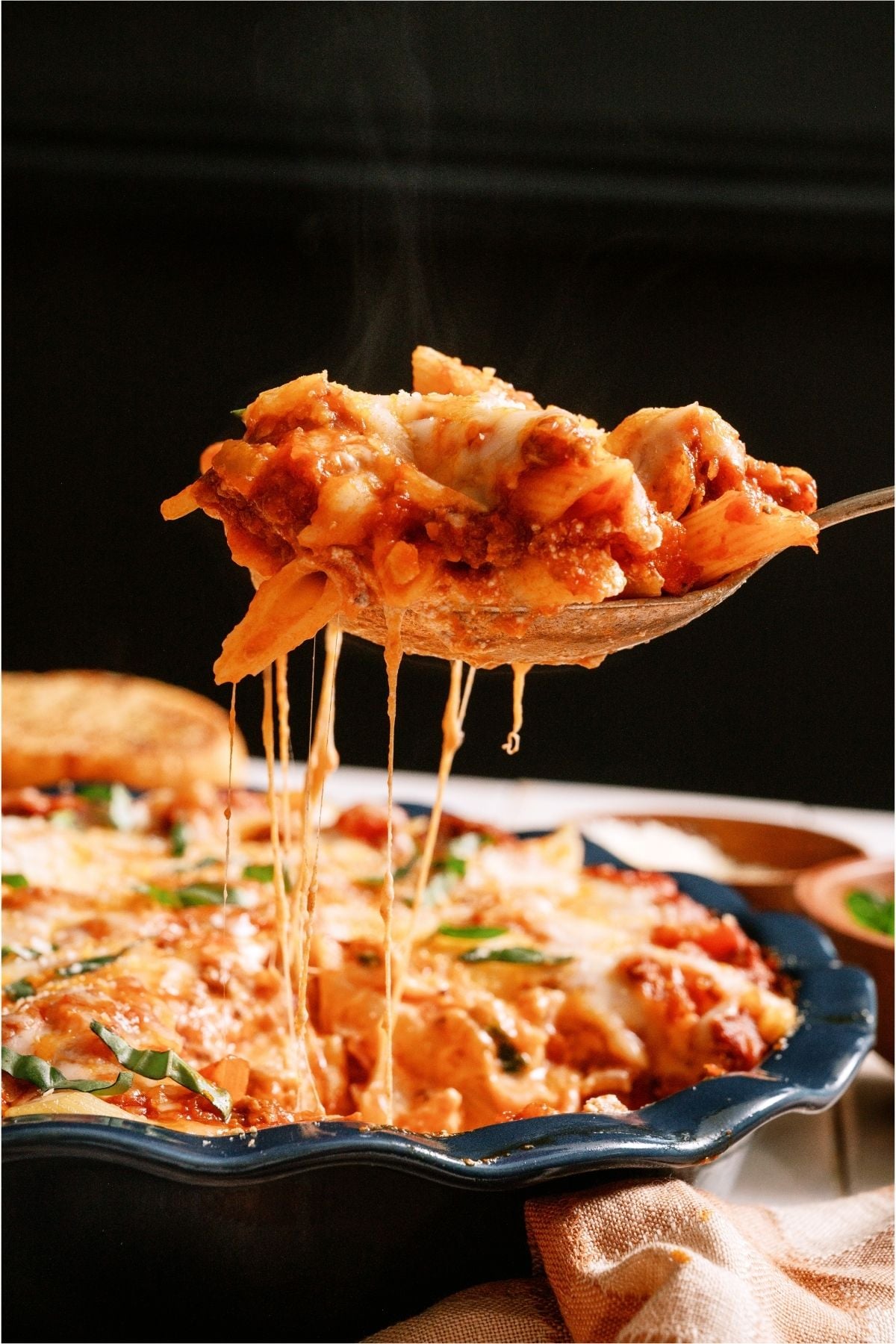 A spoon lifting a serving of Baked Ziti out of the baking dish.