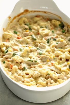 A white casserole dish filled with a pasta bake mixed with vegetables and topped with a creamy sauce.