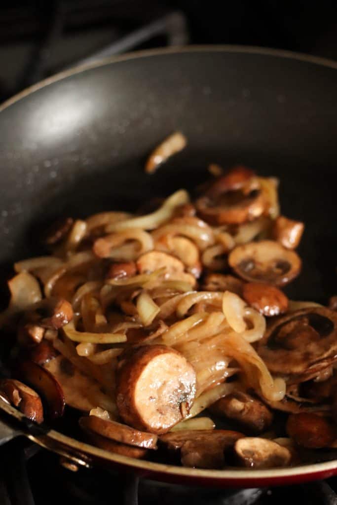 Mushrooms and onions sautéed in a skillet.