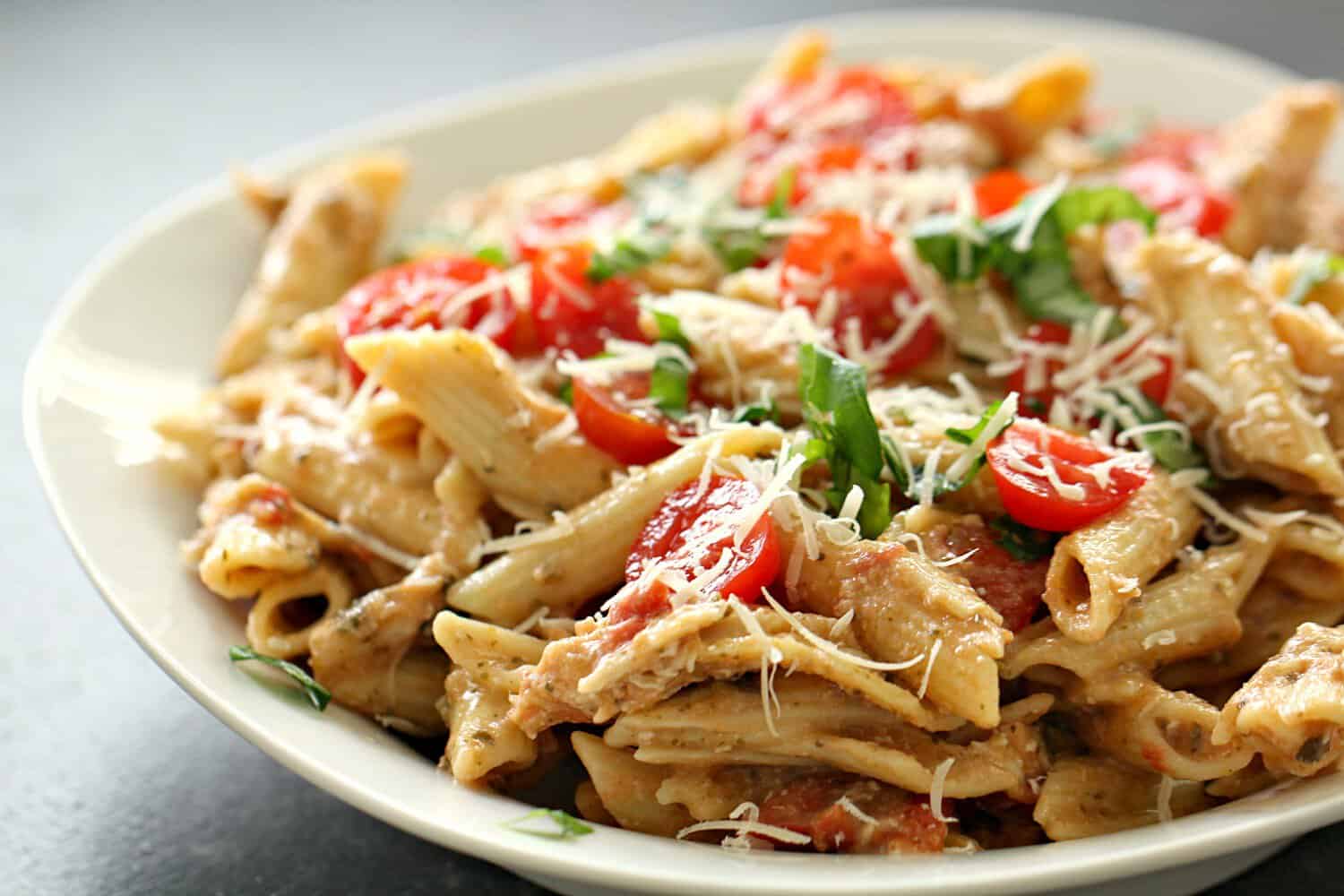 Slow Cooker Alfredo Pesto Chicken and Pasta on a white dinner plate topped with tomatoes and cheese