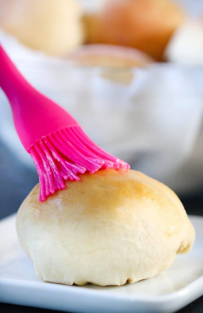 A brush brushing butter on a roll.