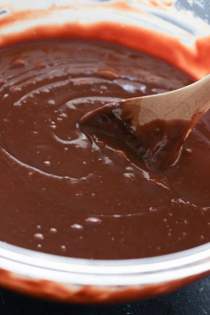 Adding chocolate sauce to mixing bowl and stirring with a wooden spoon.
