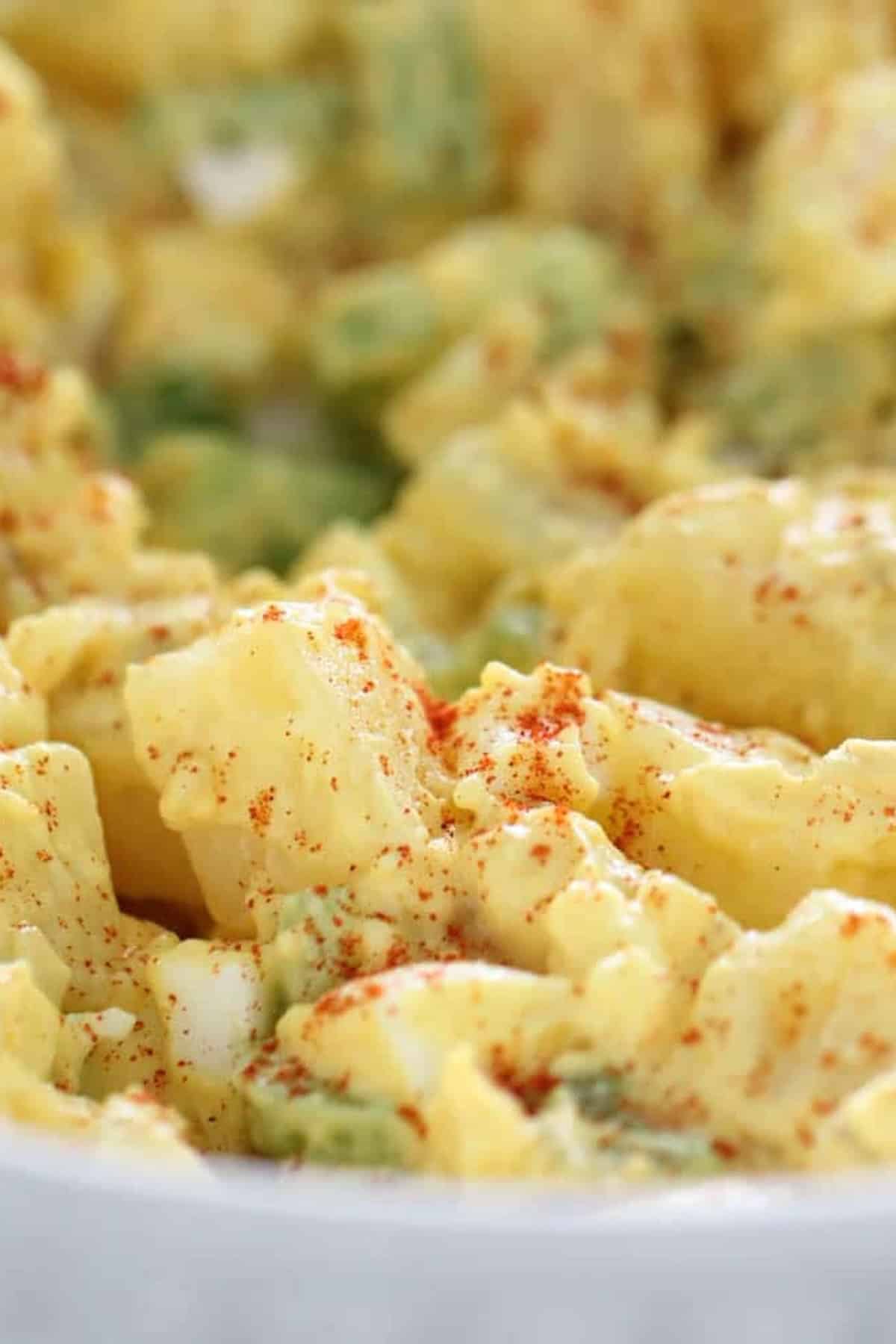 Close-up of creamy potato salad with cubed potatoes, avocado, and a light sprinkling of paprika.