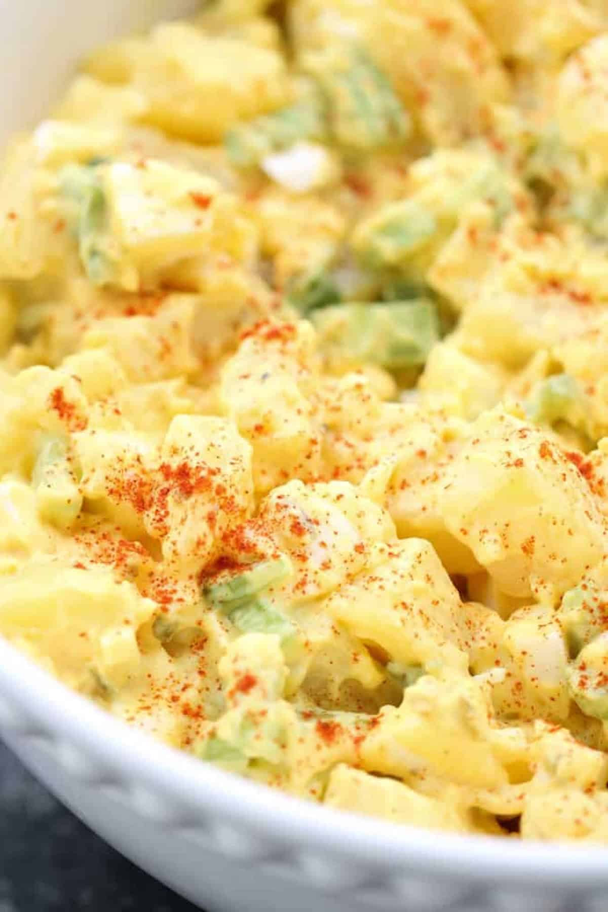 Potato salad with diced potatoes, green onions, and a creamy dressing, garnished with a sprinkle of paprika.