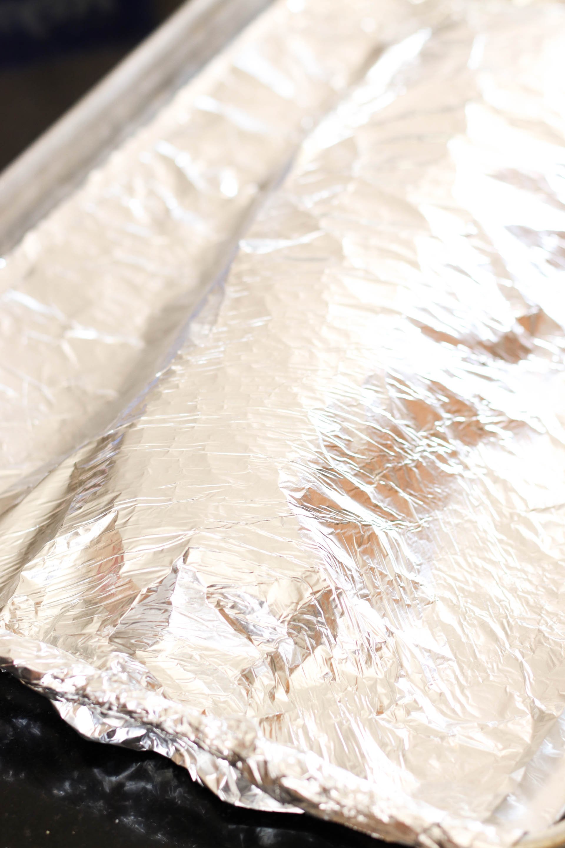 Foil Lined baking sheet with uncooked ribs on them covered with foil