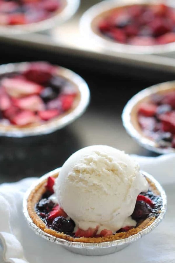 Mini Berry Pies on a table with one topped with ice cream.