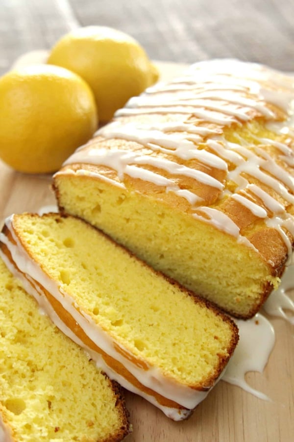 Starbucks Copycat Lemon Pound Cake on a serving plate sliced with lemons in the background.