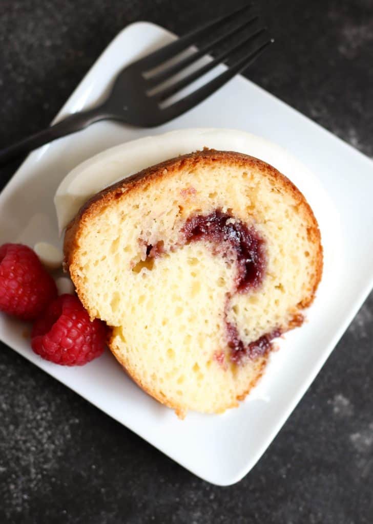 A slice of White Chocolate Raspberry Bundt Cake on a white dish with fresh raspberries and a fork.