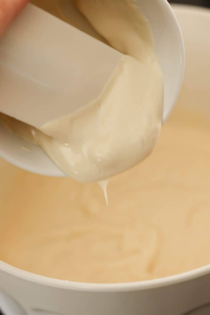A spatula scraping a measuring cup of sour cream into a mixing bowl.