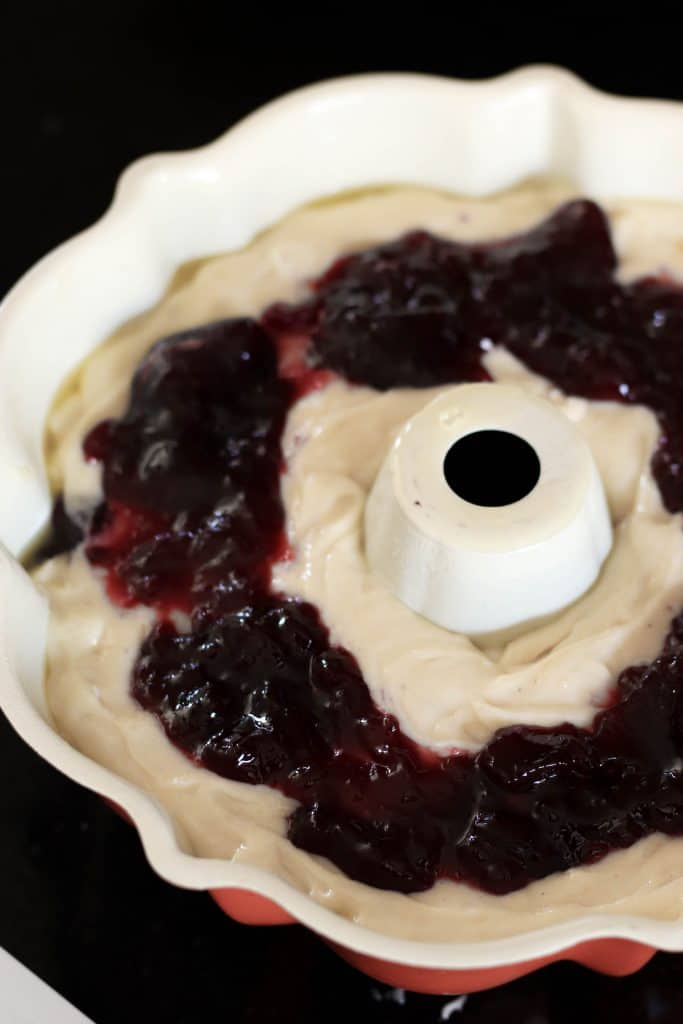 A layer of raspberry jam spread on top of white cake batter in a bundt cake pan.