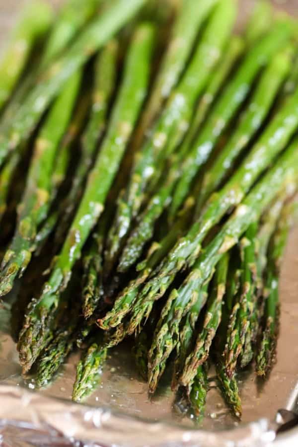 A close-up of roasted asparagus spears arranged on a sheet of aluminum foil.