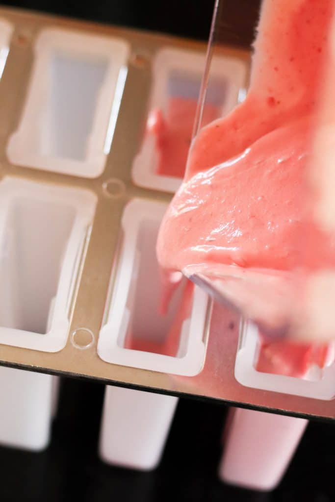Pouring strawberry mixture into popsicle molds.