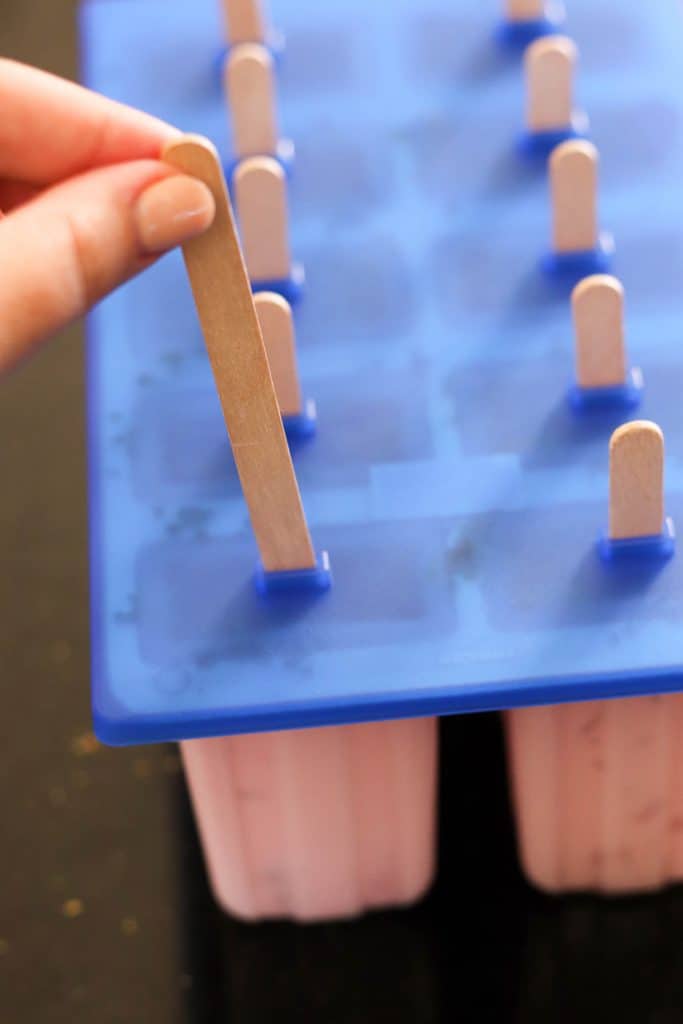 Inserting popsicle sticks into popsicle mold.