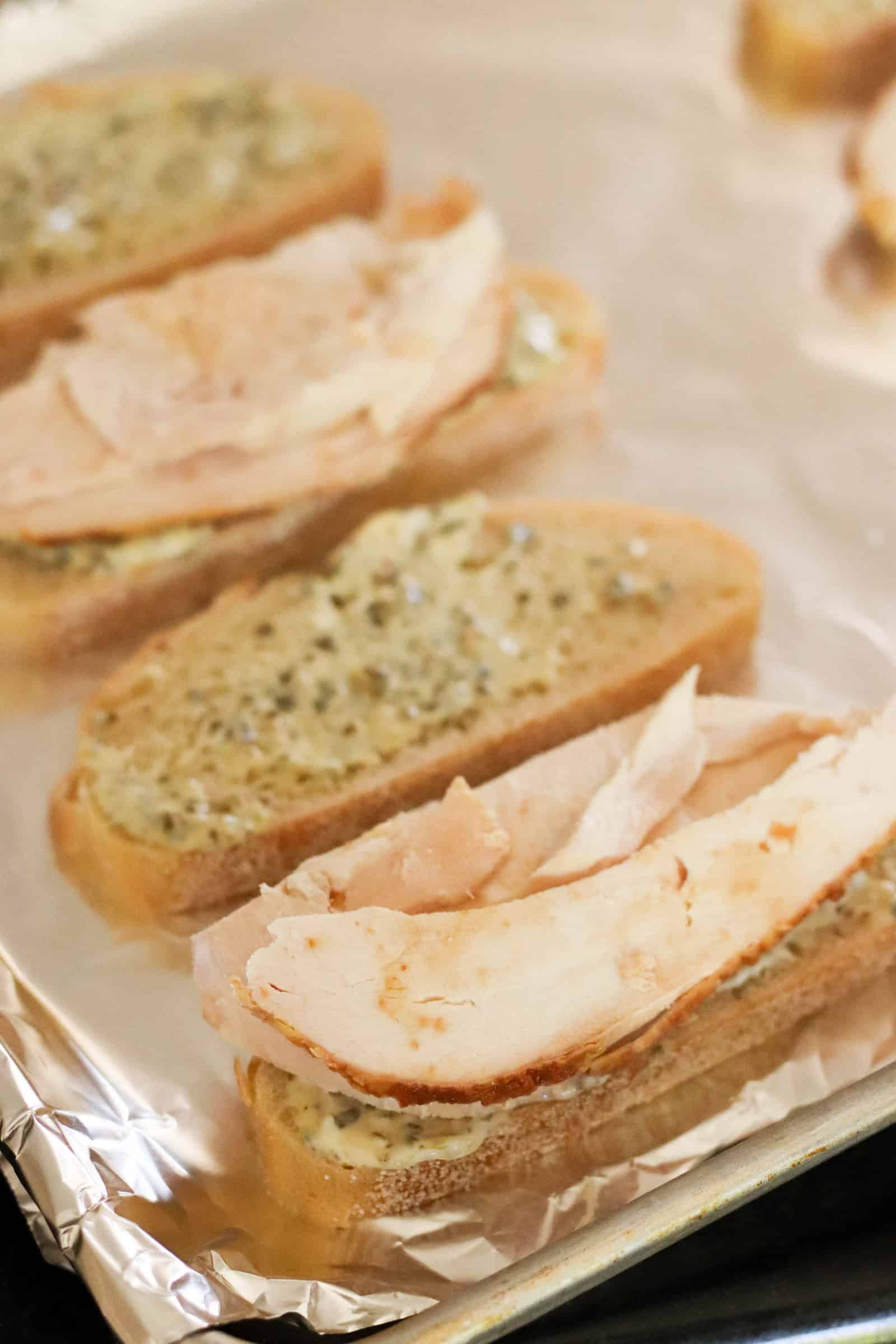 Sliced bread topped with Pesto Mixture and chicken on a foil lined baking sheet