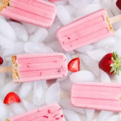 Strawberry Cheesecake Popsicles laying on ice cubes with fresh strawberries.