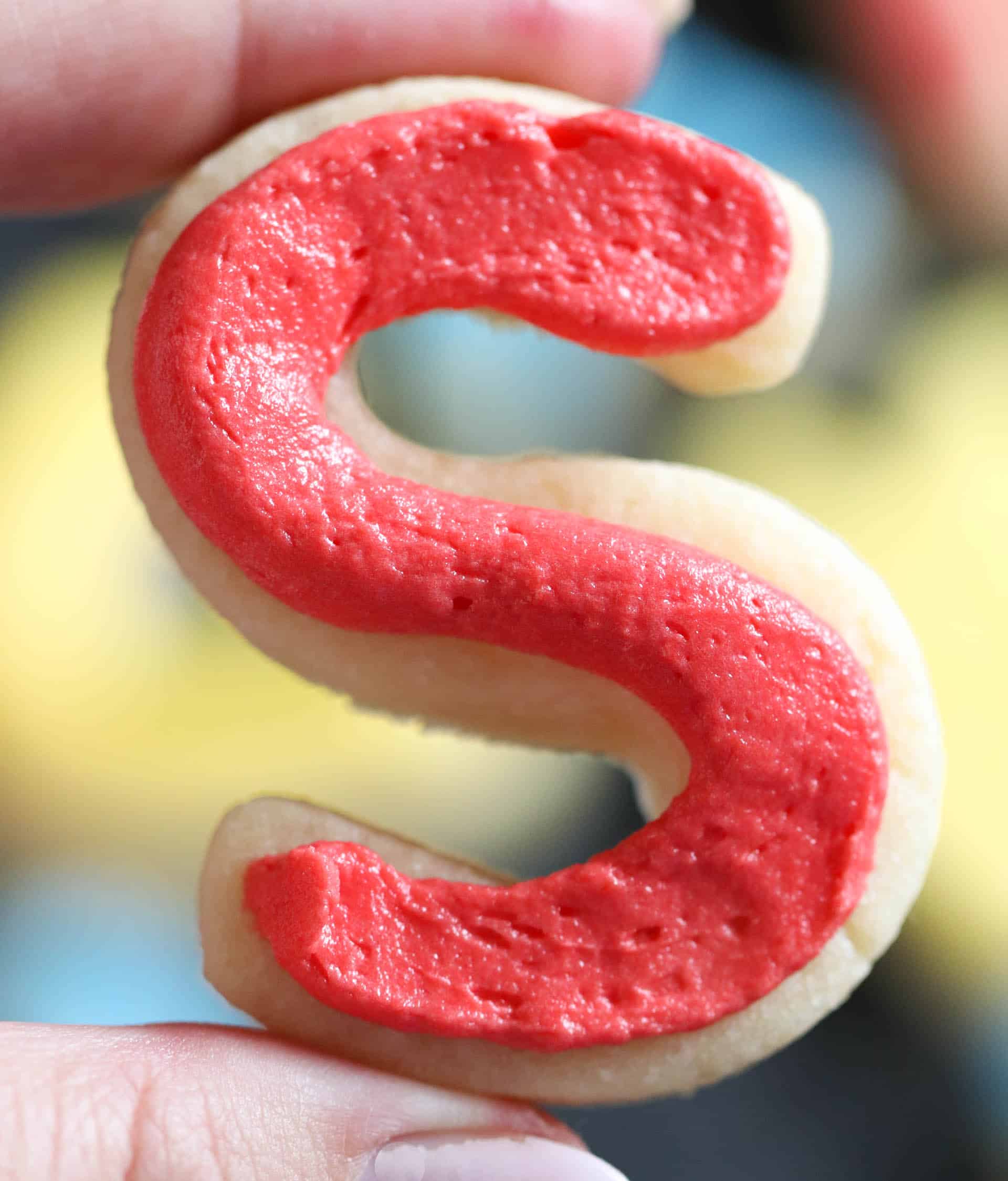 A sugar cookie shaped like the letter S frosted with red buttercream frosting.