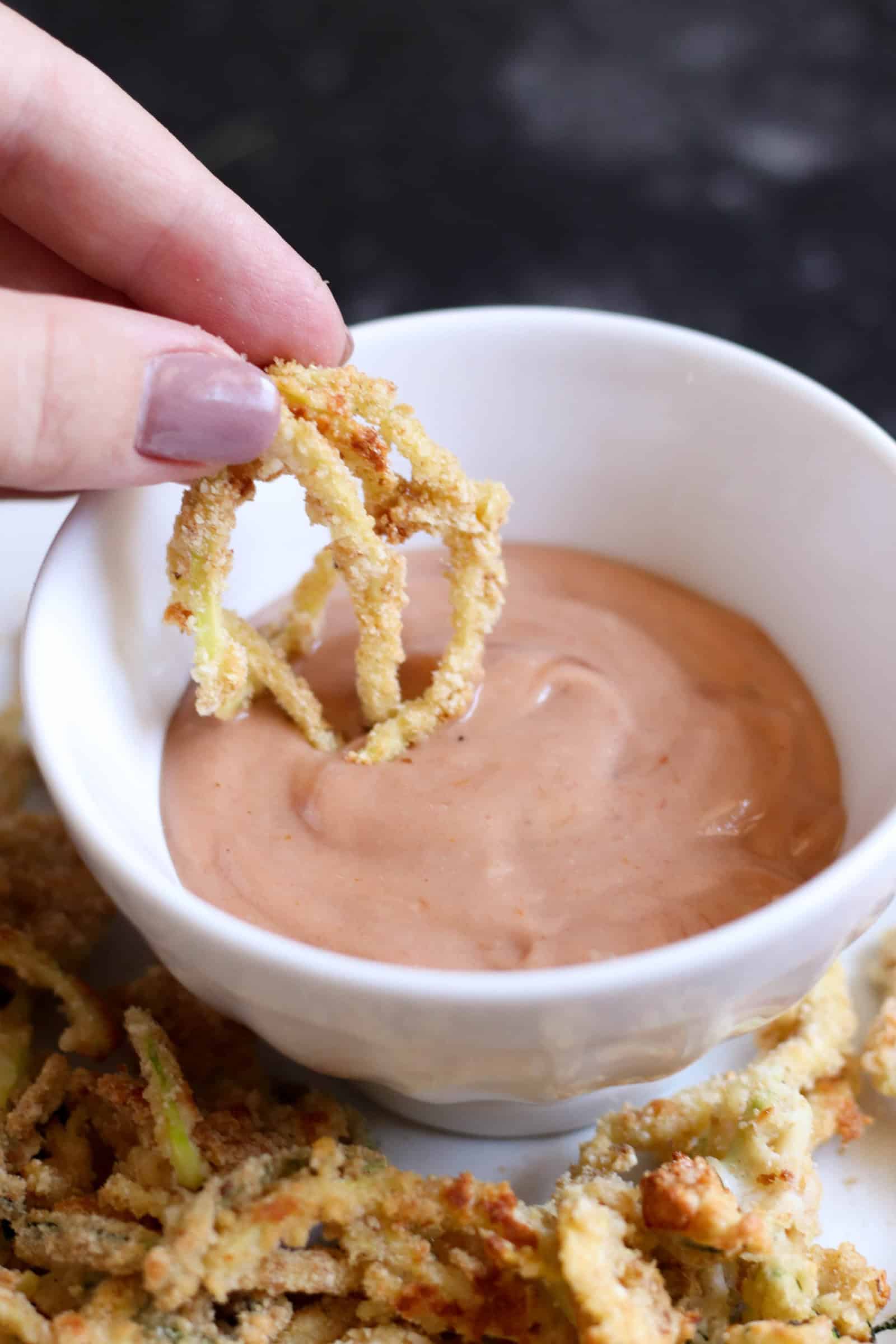 Baked Parmesan Zucchini Strings dipped in small bowl of fry sauce