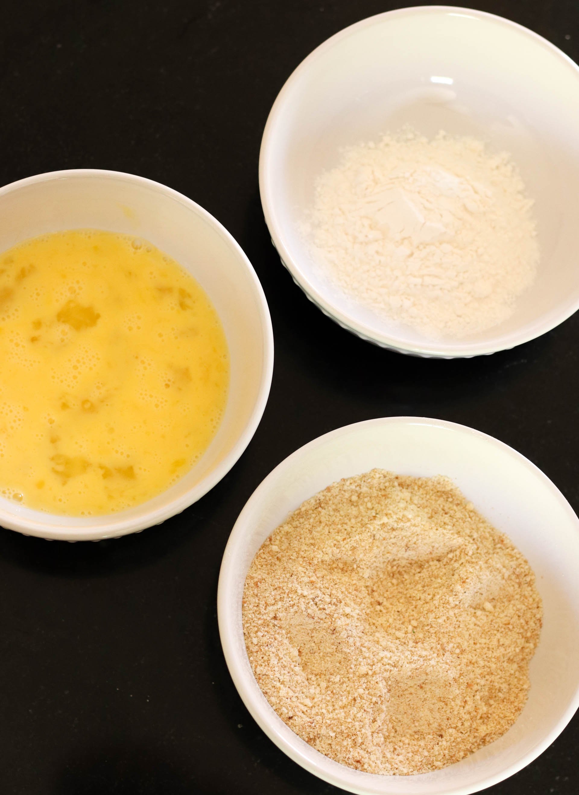 3 shallow bowls, one filled with eggs, one filled with breadcrumbs, one filled with flour