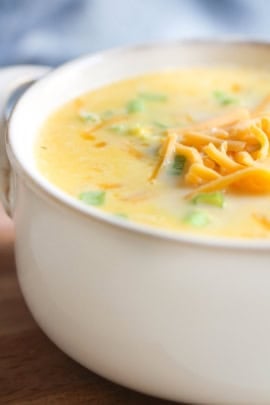 A close-up of a bowl of creamy soup garnished with shredded cheese and chopped green onions.